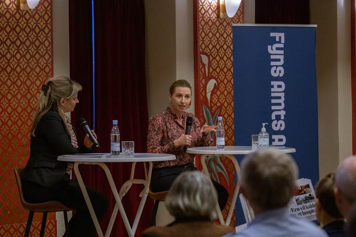 Statsminister Mette Frederiksen sidder ved et rundt bord. I hånden har hun en mikrofon, hvorfra hun svarer på spørgsmål fra Fyns Amts Avis' læsere. 