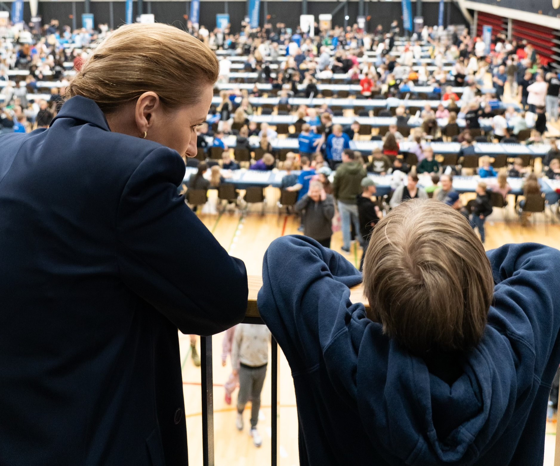 Statsminister Mette Frederiksen ved siden af en skoleelev der skuer ud mod deltagerne til Landsfinalen i Skolernes Skakdag