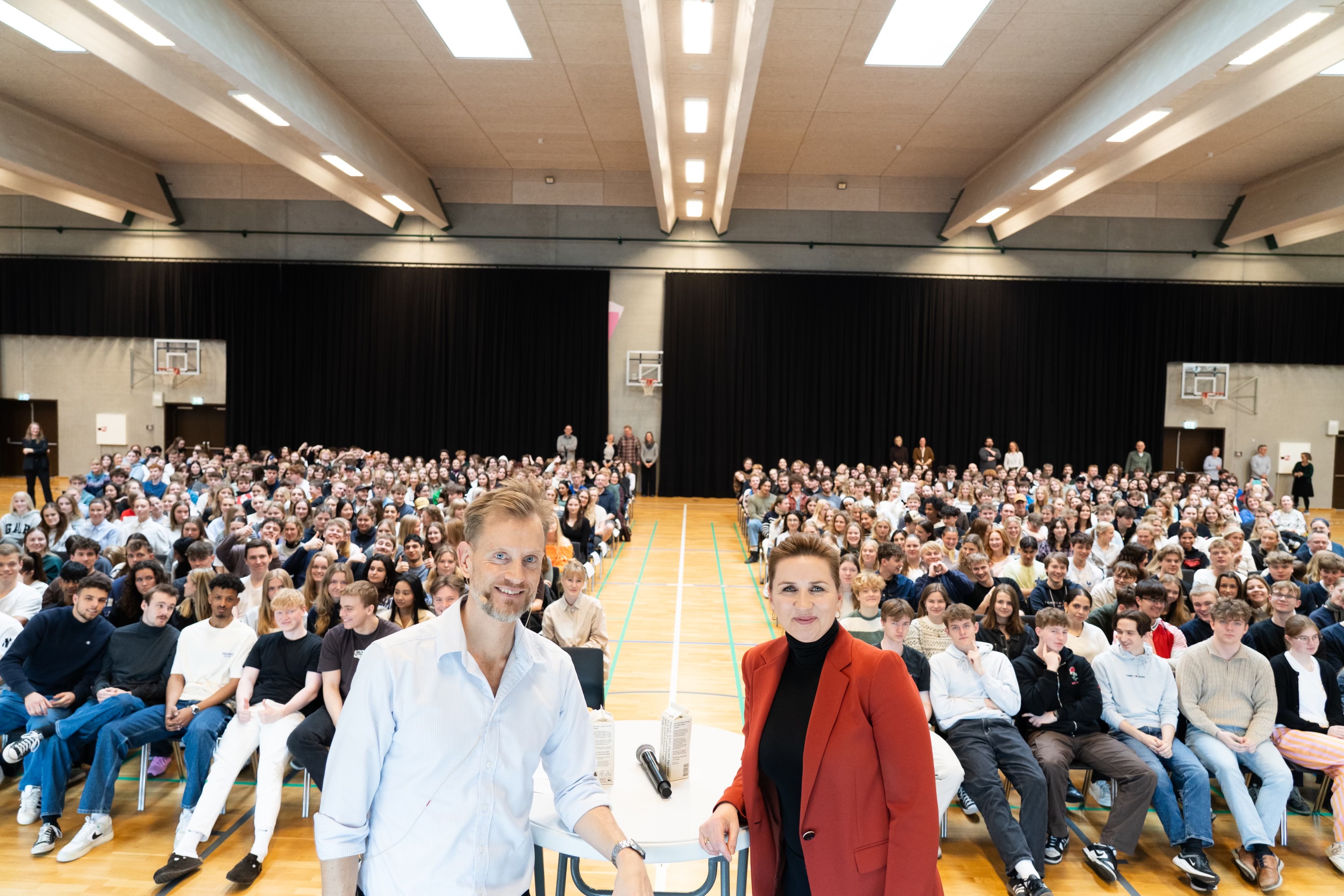 Statsminister Mette Frederiksen med rektoren fra gymnasiet, med elever fra gymnasiet i baggrunden