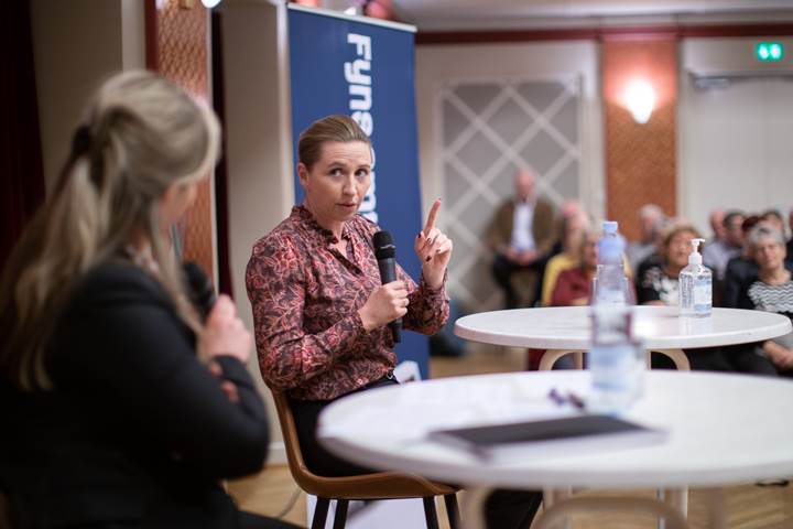 Statsminister Mette Frederiksen sidder ved et rundt bord. I hånden har hun en mikrofon, hvorfra hun svarer på spørgsmål fra Fyns Amts Avis' læsere. 